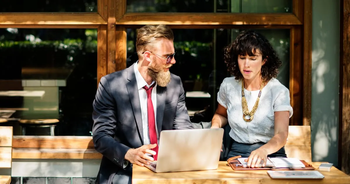 Two colleagues reviewing documents and a laptop together at an outdoor table