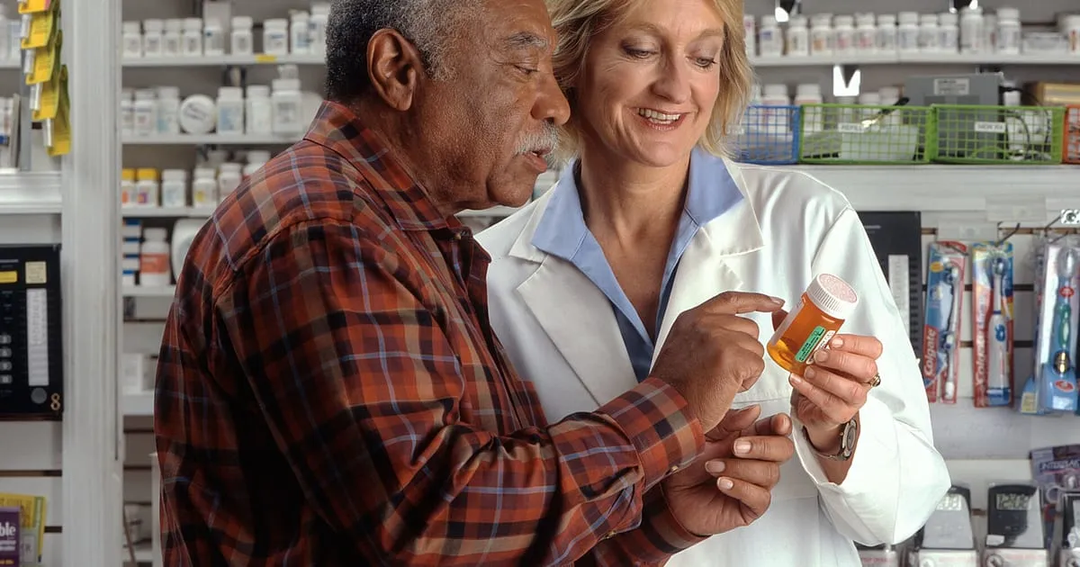 An older man reviewing a prescription bottle with a pharmacist in a pharmacy