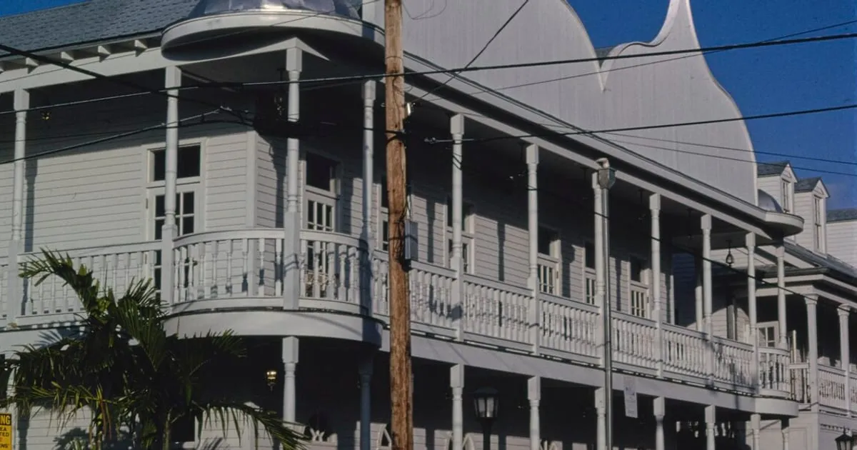 A two-storey white wooden apartment building with wraparound balconies and a palm tree in Key West, Florida